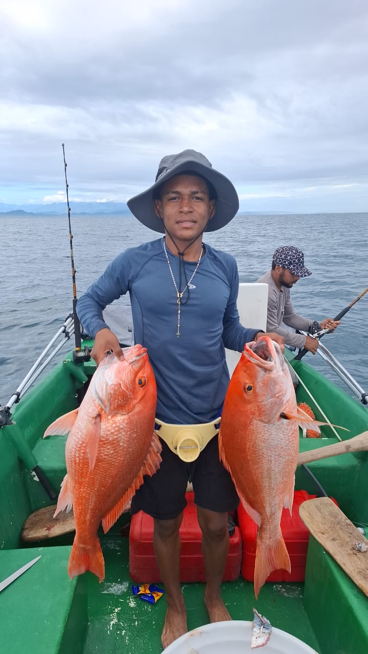 Local fisherman holding two fresh red snappers on a boat in Cahuita waters