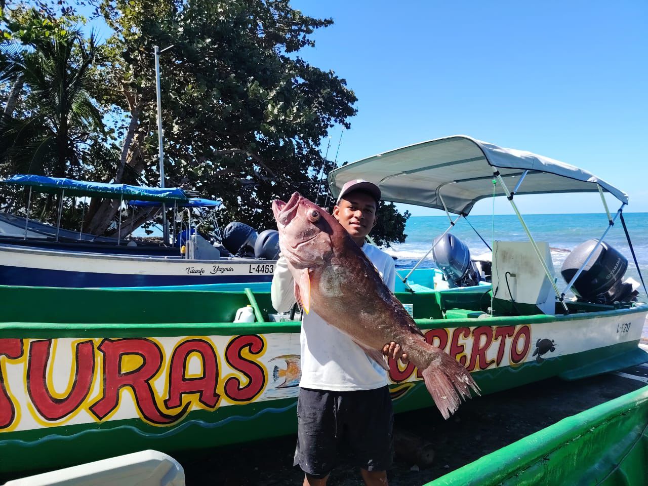 Young fisher holding a large catch by the boats
